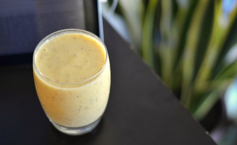 Mango smoothie on brown desk with green plant in background.