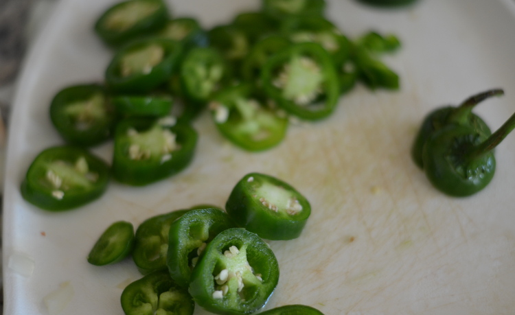 Jalapeno sliced into wheels on white cutting board for five alarm chili
