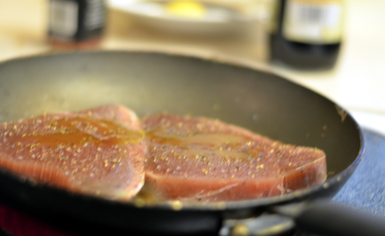 Ahi Tuna Steak seasoned and cooking on fry pan with soy sauce and lemon chili peppers in background