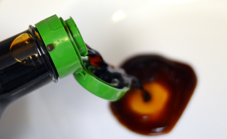 Pouring soy sauce into white bowl to start spicy soy fish sauce recipe