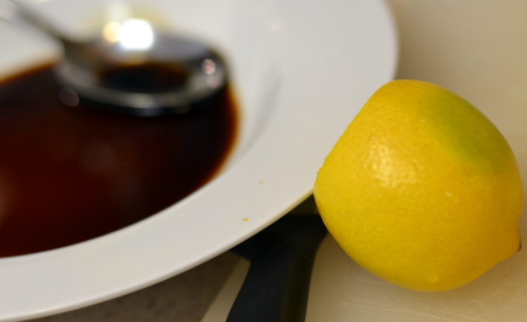 Dark brown spicy soy fish sauce in white bowl with whole lemon on side