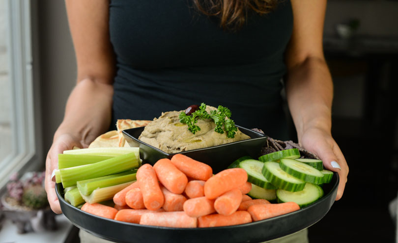 Black olive hummus served on a platter with veggies and pita and chips by Shalva.