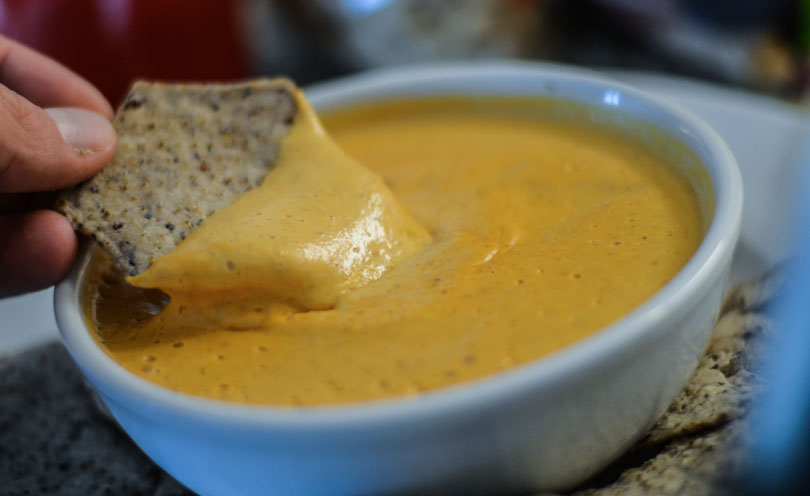 A chip being dipped into hot cashew queso dip.