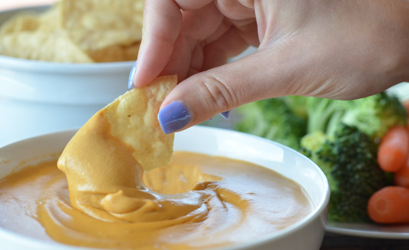 Pretty, painted lady fingers dipping a tortilla chip into a bowl of cashew queso.