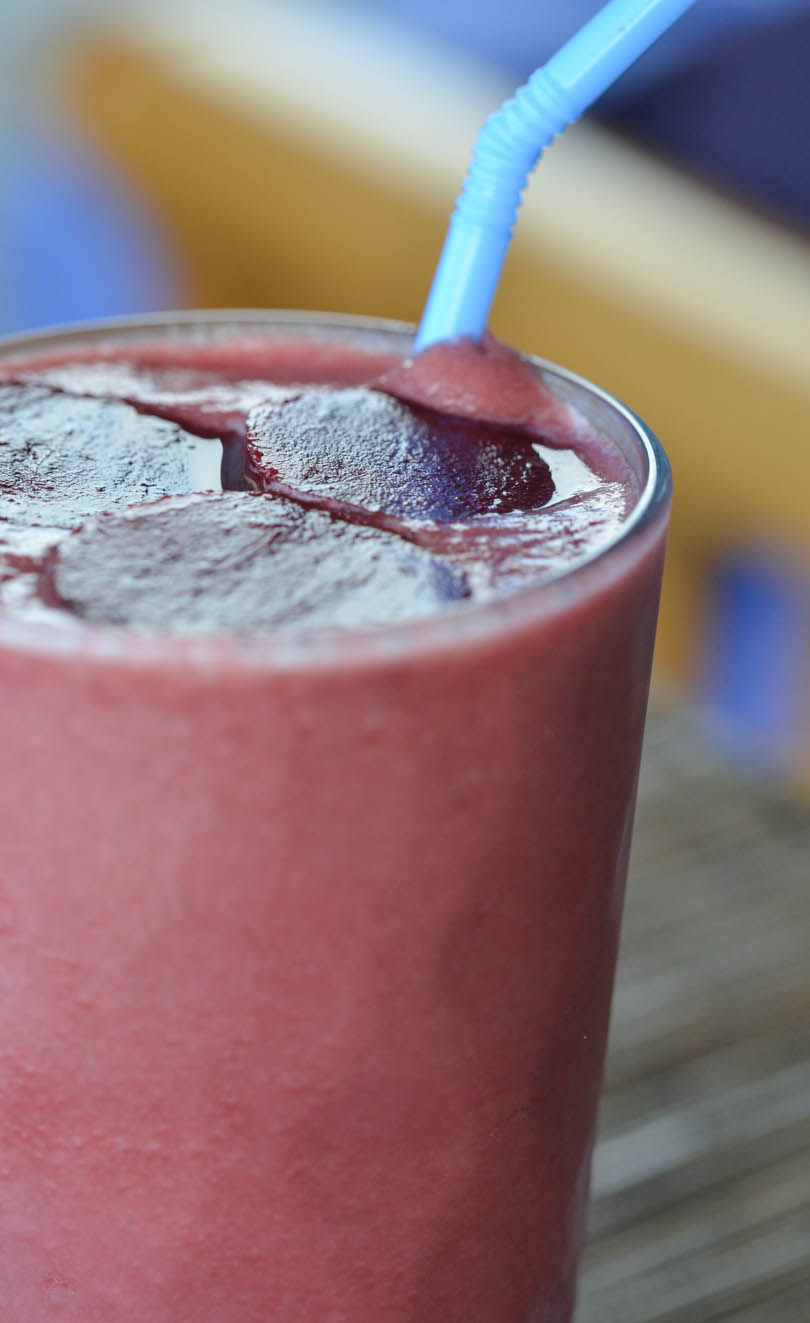 Bloody apple beet smoothie with a blue straw.