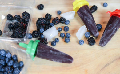 Three blueberry blackberry popsicles and their ingredients on cutting board.