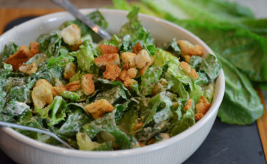 Caesar dressing served with romaine in a big white bowl.