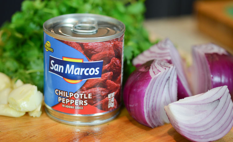 Can of San Marcos chipotle peppers next to red onion and cilantro.