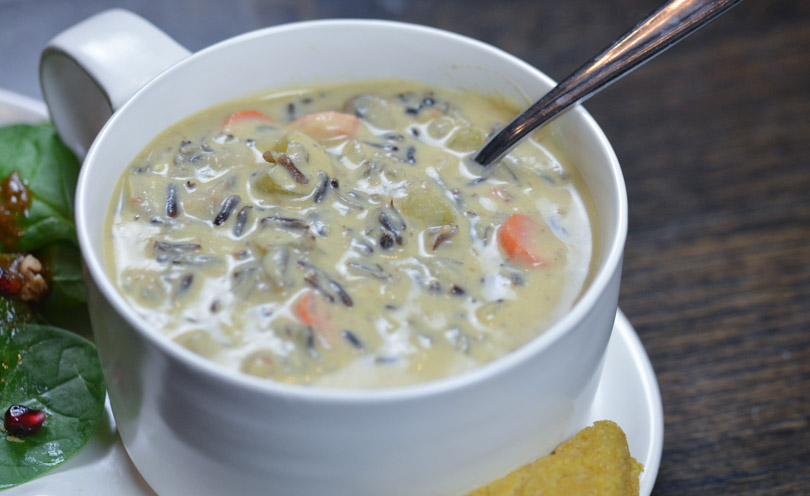 Vegan, creamy wild rice soup in large bowl served with salad and corn bread.