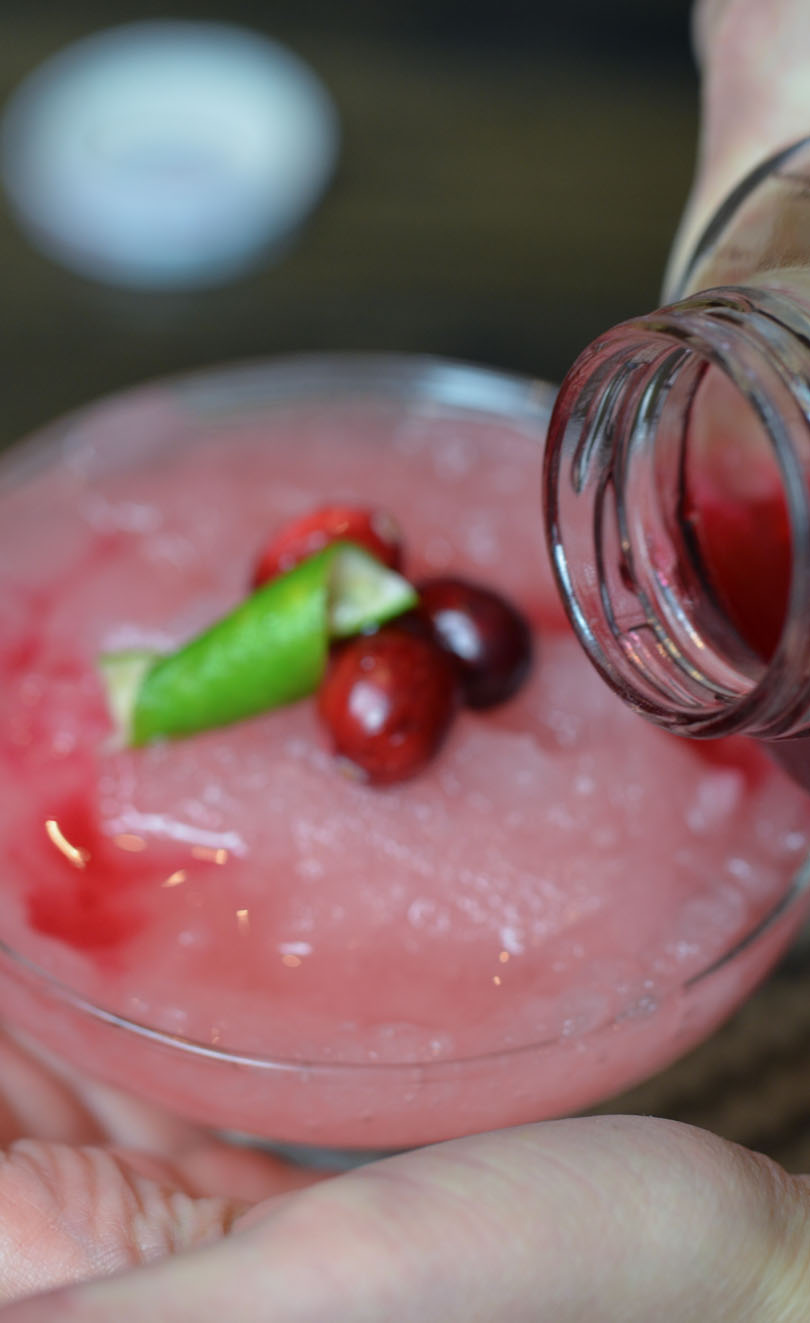 Pouring cranberry juice into the glass over frozen merry mule drink.