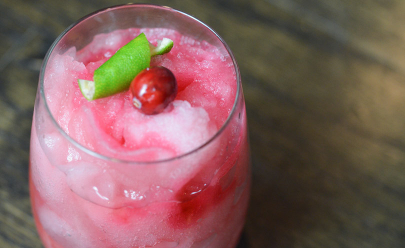 Merry mule, a frozen, pink beverage garnished with cranberry and lime garnish.