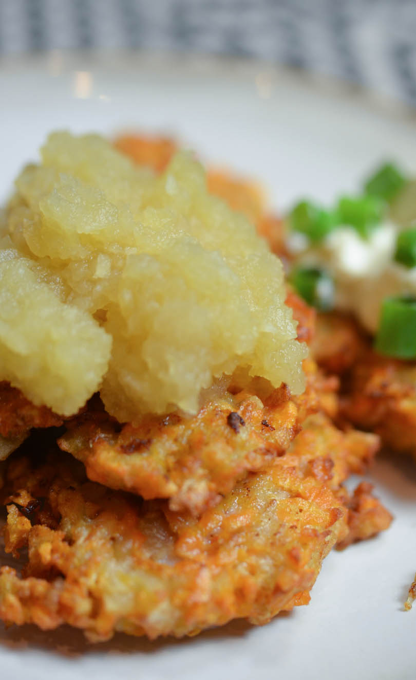 Sweet potato latkes with apple sauce on top and sour cream in background.