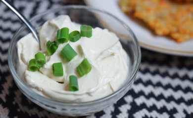 Vegan sour cream with chives on top served with sweet potato latkes in background.
