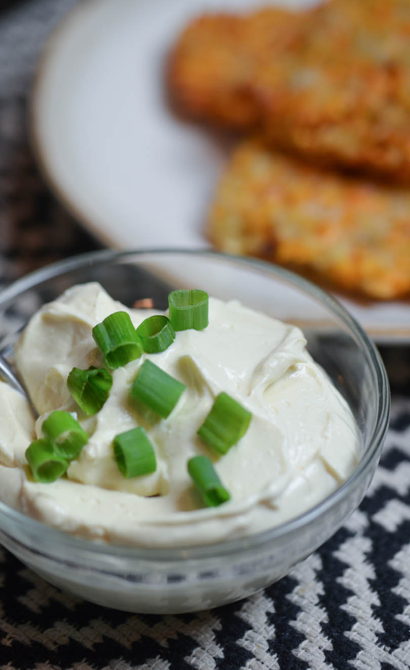 Vegan sour cream from with chives on top and latkes in background.