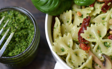 Jar of vegan pesto next to pesto-covered bow tie pasta.