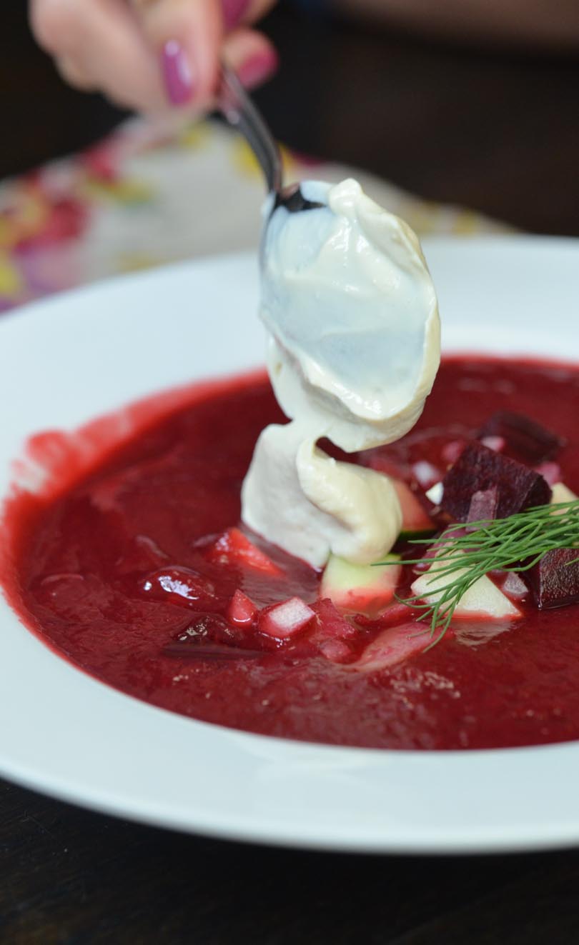 A dollop of vegan sour cream onto a bowl of cold beet borscht .