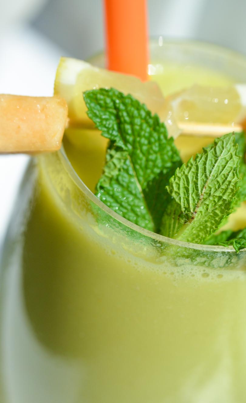 A tall glass of guts juice garnished with cantaloupe and mint.