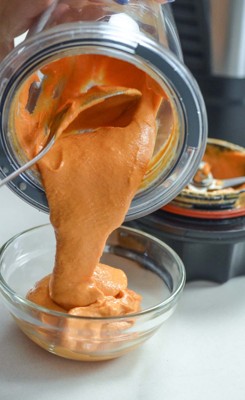 Roasted red pepper hummus being poured from a 20 oz Vitamix container.
