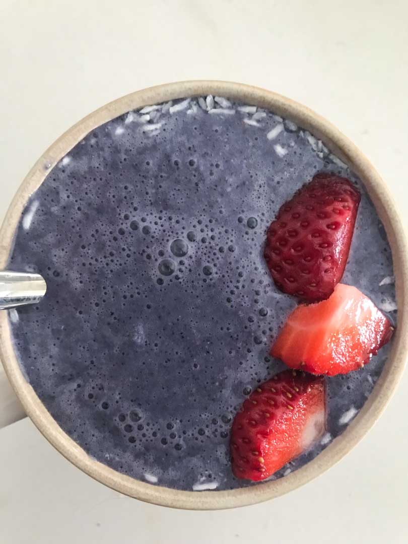 Blueberry protein shake in a cup with strawberries on top.