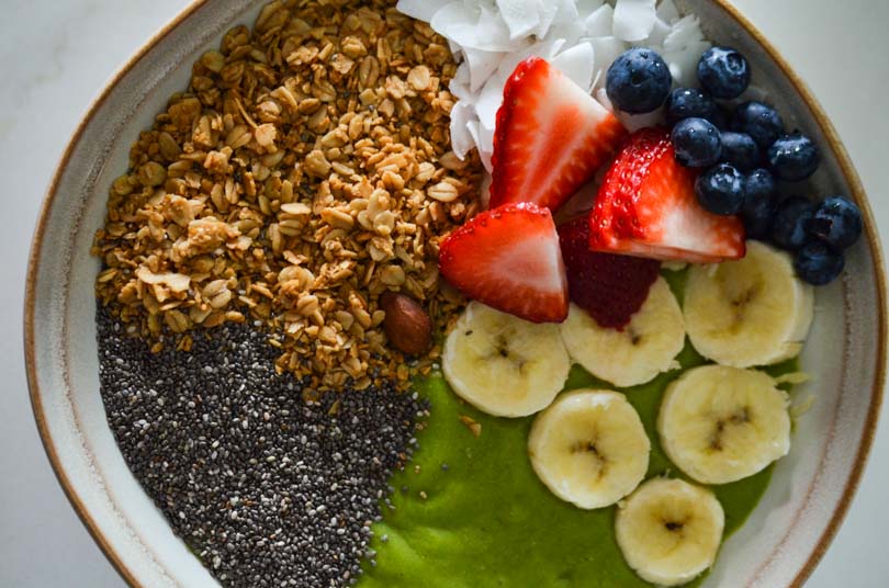 Green smoothie bowl with granola, strawberries, blueberries, banana, and chia seeds.