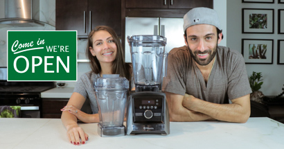 Shalva and Lenny Gale with Vitamix A3500 and 48 oz container for Life is No Yoke with a "come we're open" sign.